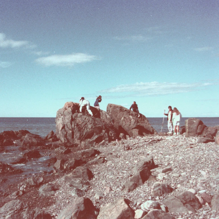 Family photo from a rocky beach in Cape Breton, showing my dad, siblings, and cousins among large shoreline rocks with the ocean beyond. Landscapes that shape a lifelong sense of place.